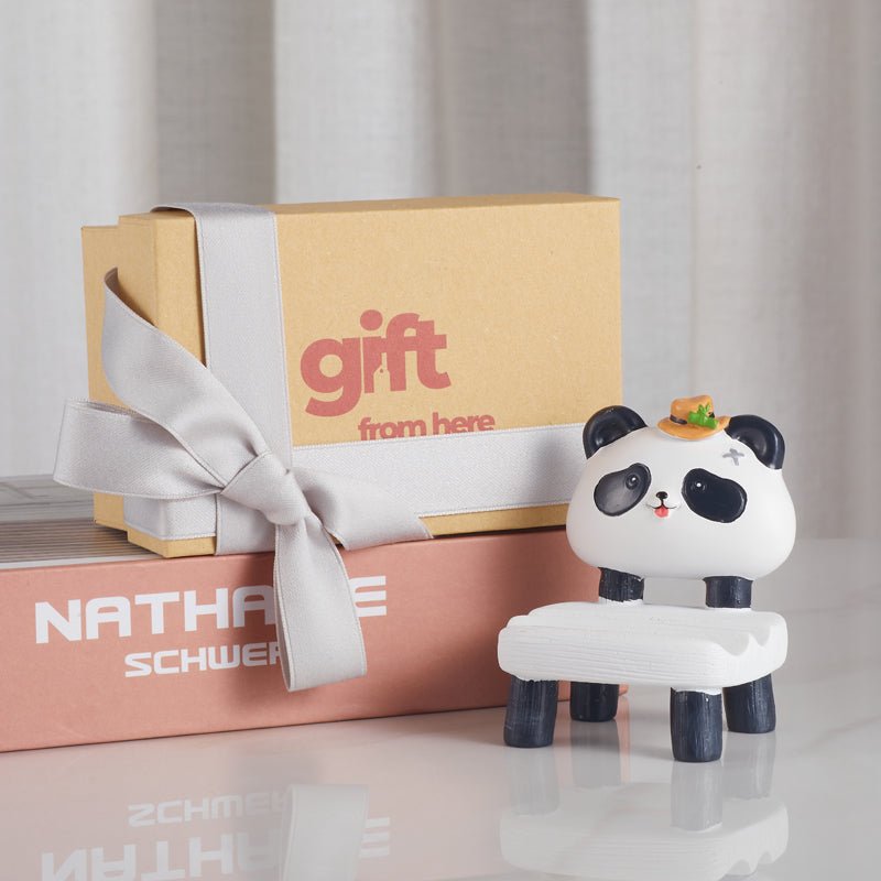 Panda-shaped phone holder with a hat next to a gift box with a ribbon